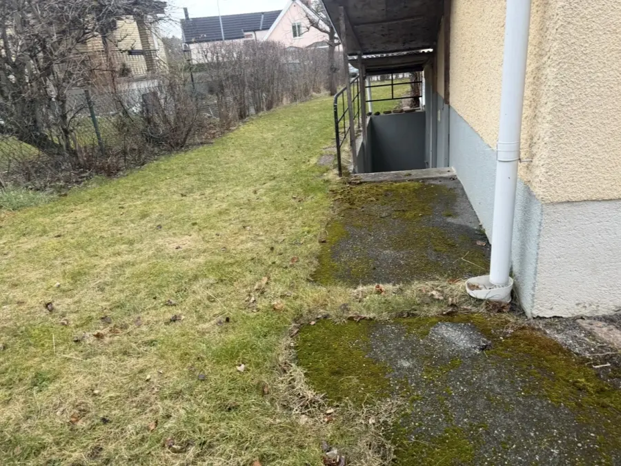 Mossbelupen och ojämn asfaltgång längs husgrund innan omläggning